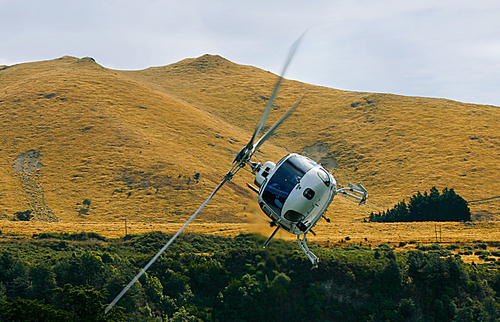 A white helicopter flying and banking around turning in a valley surrounded by mountains