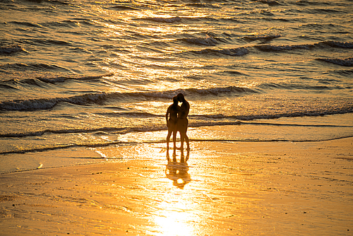 Silhouettes of people walking on beach and taking photo at beautiful sunset