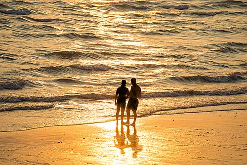 Silhouettes of people walking on beach and taking photo at beautiful sunset