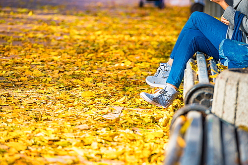 Young woman sitting on a bench in autumn park with yellow fallen leaves