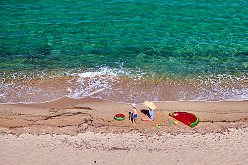 Two year old toddler boy and his mother on beach with inflatable float and ring. Summer family vacation. Sithonia, Greece.