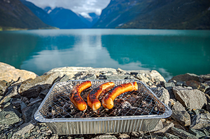 Grilling sausages on disposable barbecue grid. Beautiful Nature Norway natural landscape.