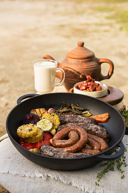 grilled meat sausages with s and spices, milk and teapot on background