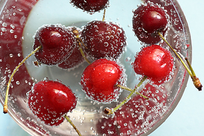 Glass of water and fresh cherries with bubbles