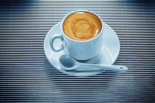 Cup of coffee saucer teaspoon on striped background.