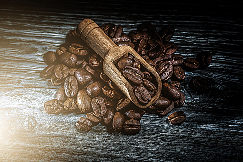 Roasted coffee seeds in scoop on wooden board.
