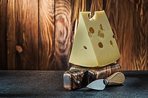 big piece of milk maasdam cheese with knife on little vintage wooden cutting board wooden background