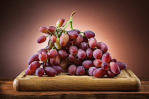 grape on wooden cutting board and brown gradient background
