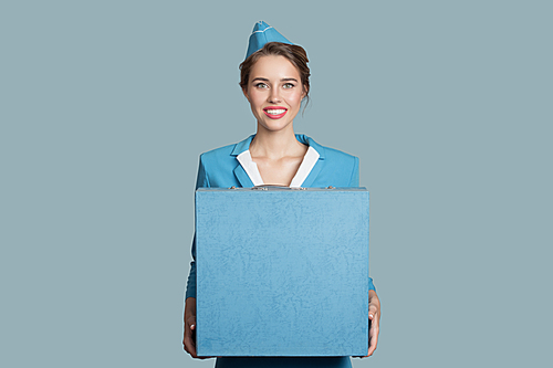 Beautiful charming stewardess holding blue box luggage in hands.