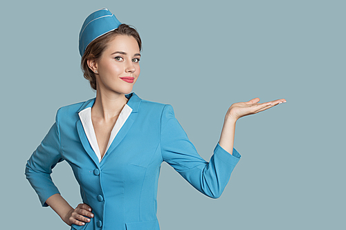 Beautiful stewardess holding blank on her hand. Blue background.