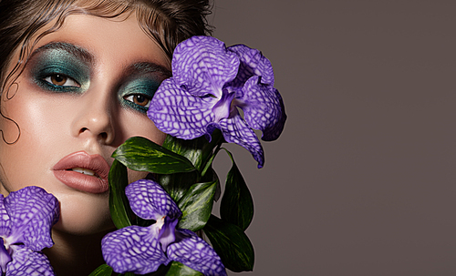 Fashion portrait of beautiful woman with bright make up and orchid near face.