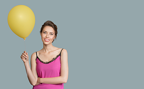 Portrait of smiling woman. Holding yellow balloon in her hand. Blue background.
