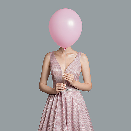 Portrait of woman im evening dress. Hides her face behind pink balloon.