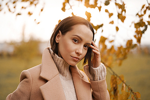Outdoor fashion photo of young beautiful lady in beige coat in autumn landscape