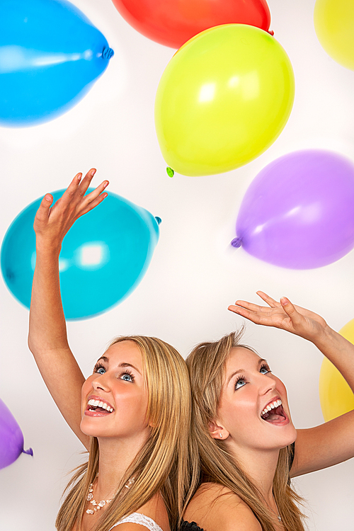 Two beautiful happy teenage girls, female young women, celebrating or at a party with colorful balloons
