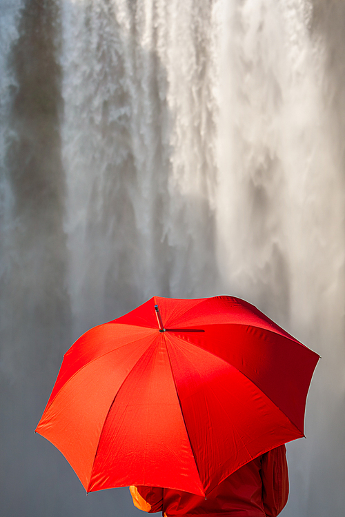 Young woman person in a red coat or jacket holding a red umbrella in front of a waterfall