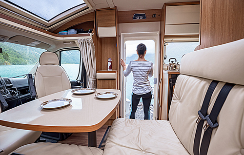 Woman in the interior of a camper RV motorhome with a cup of coffee looking at nature.