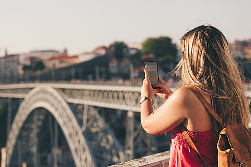 Young woman tourist enjoying beautiful landscape view on the old town with river and famous iron bridge during the sunset in Porto city, Portugal