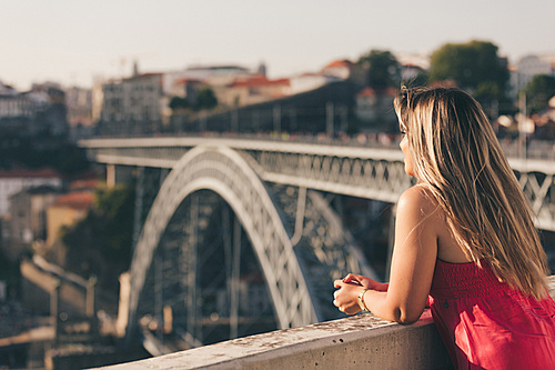 Young woman tourist enjoying beautiful landscape view on the old town with river and famous iron bridge during the sunset in Porto city, Portugal