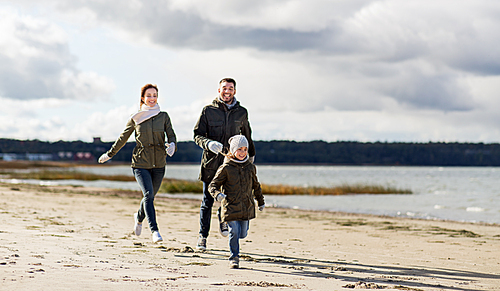 family, leisure and people concept - happy mother, father and little daughter running along autumn beach