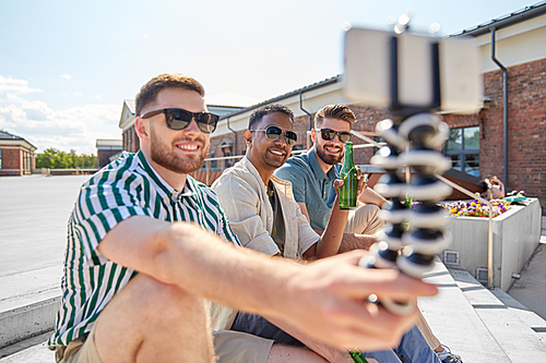 leisure, technology and people concept - happy male friends taking selfie by smartphone on tripod and drinking beer on street in summer
