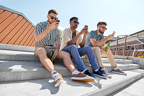 leisure, technology and people concept - happy male friends with smartphones drinking beer and talking on street in summer