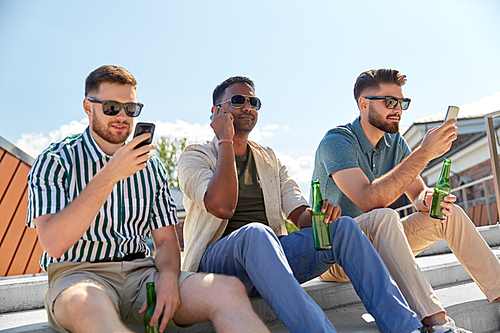 leisure, technology and people concept - happy male friends with smartphones drinking beer and talking on street in summer