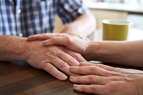 Close Up Of Woman Comforting Unhappy Senior Man Sitting In Kitchen At Home