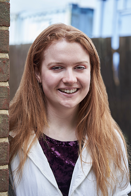 Portrait Of Smiling Teenage Girl Leaning Against Wall In Urban Setting