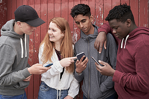 Group Of Teenage Friends Looking At Mobile Phones In Urban Setting