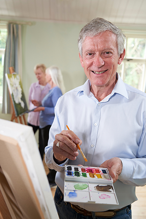 Portrait Of Senior Man Attending Painting Class With Teacher          In Background