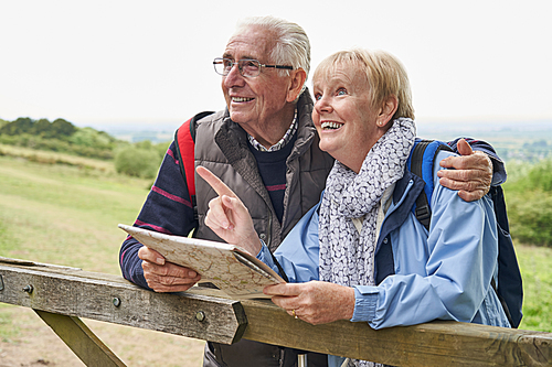 Retired Senior Couple On Walking Holiday Resting On Gate Looking At Map