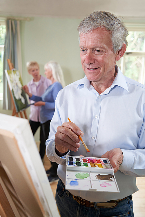 Senior Man Attending Painting Class With Teacher In Background