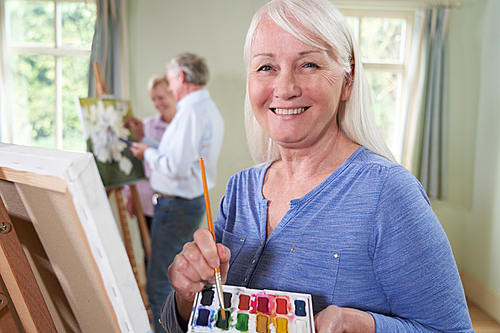 Portrait Of Senior Woman Attending Painting Class With Teacher          In Background