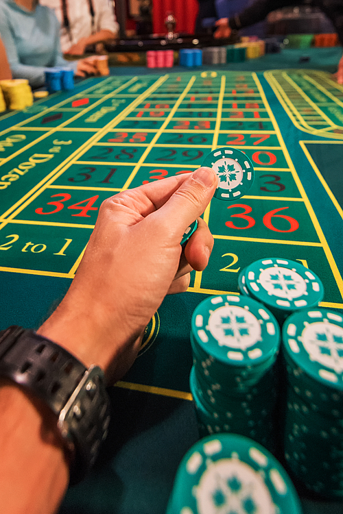 Casino, gambling and entertainment concept - male hand with stack of poker chips on a green table background