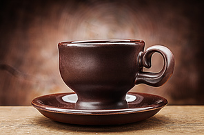 brown clay coffee cup on saucer on vintage wood background