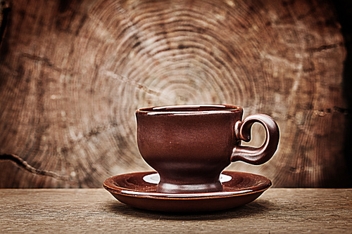single brown coffee cup on vintage wood background with cross cut of tree trunk