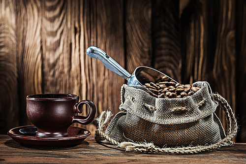 old brown clay coffee cup and sack with beans on vintage wooden background