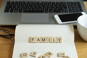 Conceptual keyword family in wooden tile letters  in personal home desk setting with laptop, notebook and accessories