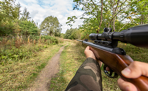 virtual reality game and violence concept - POV of male hands shooting with air rifle outdoors