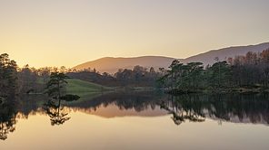 Stunning landscape image of Tarn Hows in Lake District during beautiful Autumn Fall evening sunset with vibrant colours and still waters
