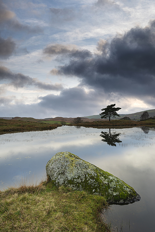 Beautiful landscape image of moody storm clouds over Kelly Hall Tarn in Lake District during late Autumn Fall afternoon