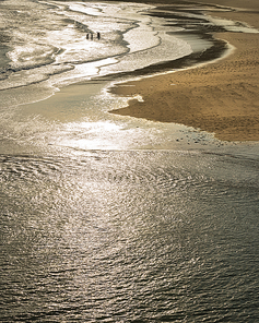 Unidentified people playing in ocean at Three Cliffs Bay in South Wales on a Summer evening