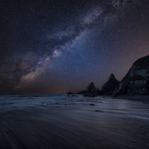 Beautiful composite landscape image of Mily Way core over sea rocks and cliffs with long exposure tide on beach