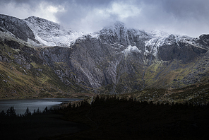 Stunning dramatic Winter landscape image of Llyn Idwal and snowcapped Glyders Mountain Range in Snowdonia