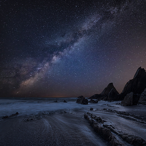 Beautiful composite landscape image of Mily Way core over sea rocks and cliffs with long exposure tide on beach