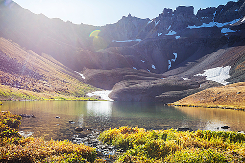 Serene scene by the mountain lake with reflection of the rocks in the calm water.