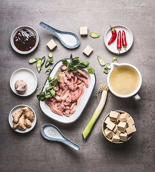 Various asian cooking ingredients in bowls for spicy asian soup with tofu and meat :  sliced meat, ginger, chili, diced tofu ,Oyster sauce, garlic and broth, top view, flat lay