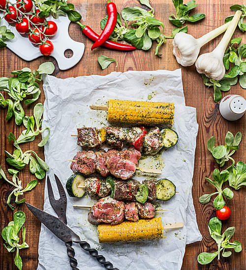 Meat Skewers  for grill with vegetables and corn ears on rustic wooden background , top view
