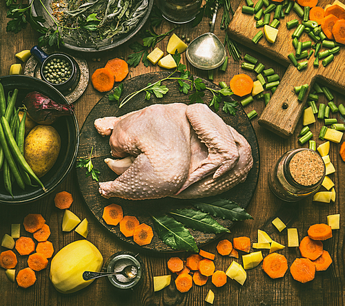Whole chicken with various healthy cooking ingredients for soup or stock : chopped vegetables, herbs and spices on rustic table background, top view. Healthy food or diet eating concept.